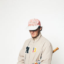 Load image into Gallery viewer, A man wearing a beige jacket with colorful graphic patches and a red-and-white striped baseball cap, photographed against a plain white background.
