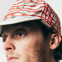 Load image into Gallery viewer, Close-up of a man wearing a white baseball cap with red embroidered lines and green lettering, shown against a plain light background.
