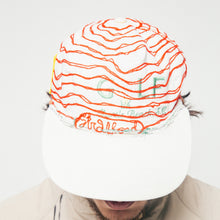 Load image into Gallery viewer, A person wearing a white baseball cap with orange scribbled line art and green text, paired with a beige zip-up jacket against a plain light background.
