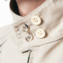 Load image into Gallery viewer, Close-up of a person wearing a light beige shirt with a high collar and decorative cream-colored buttons, against a plain white background.
