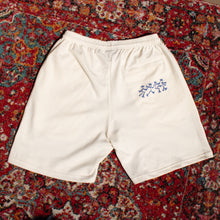Load image into Gallery viewer, White shorts with a blue design on a patterned red and multicolor rug
